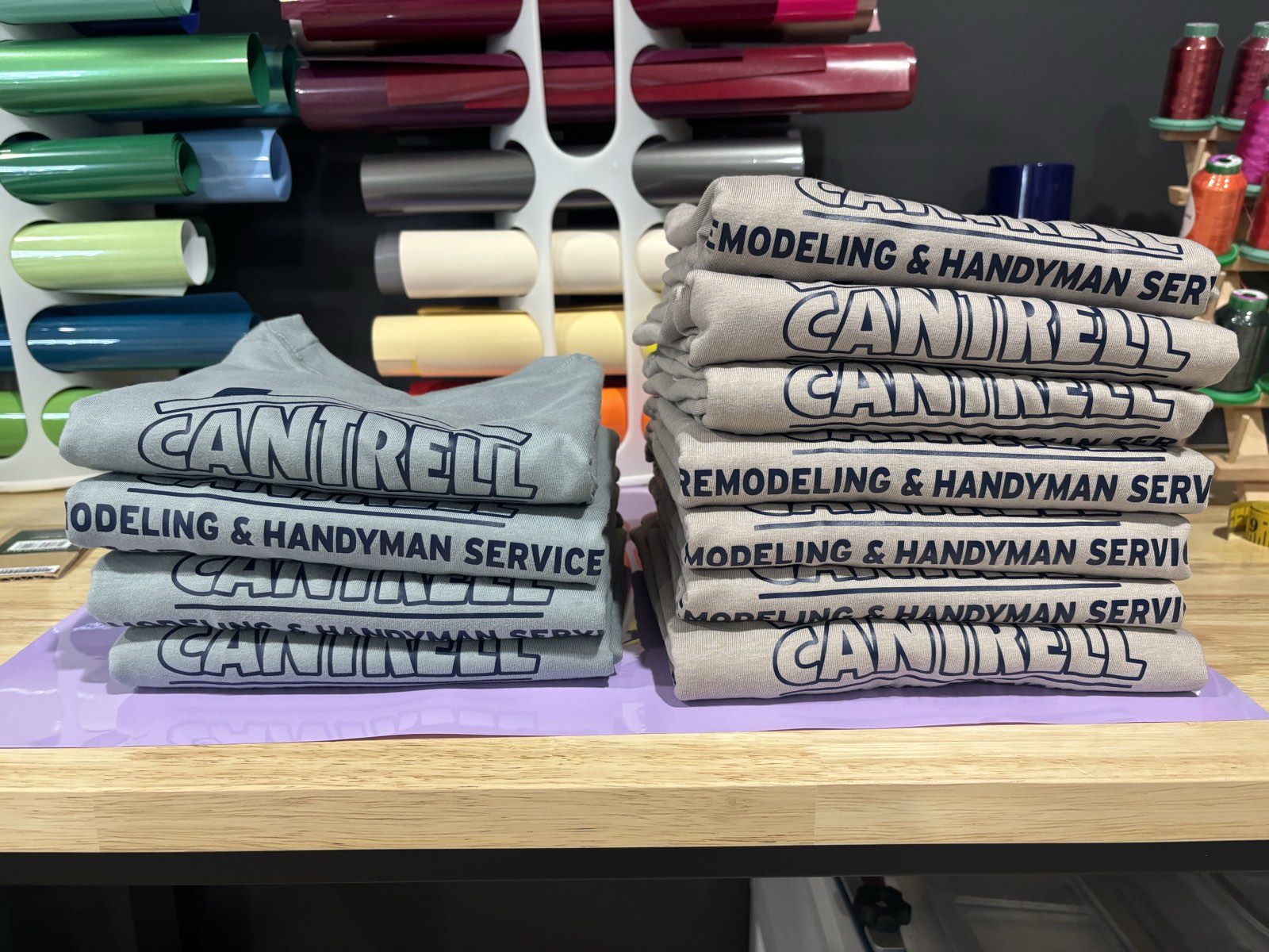 Folded stacks of freshly printed business shirts on the Thread and Press Co. worktable, with rolls of vinyl and embroidery thread behind them