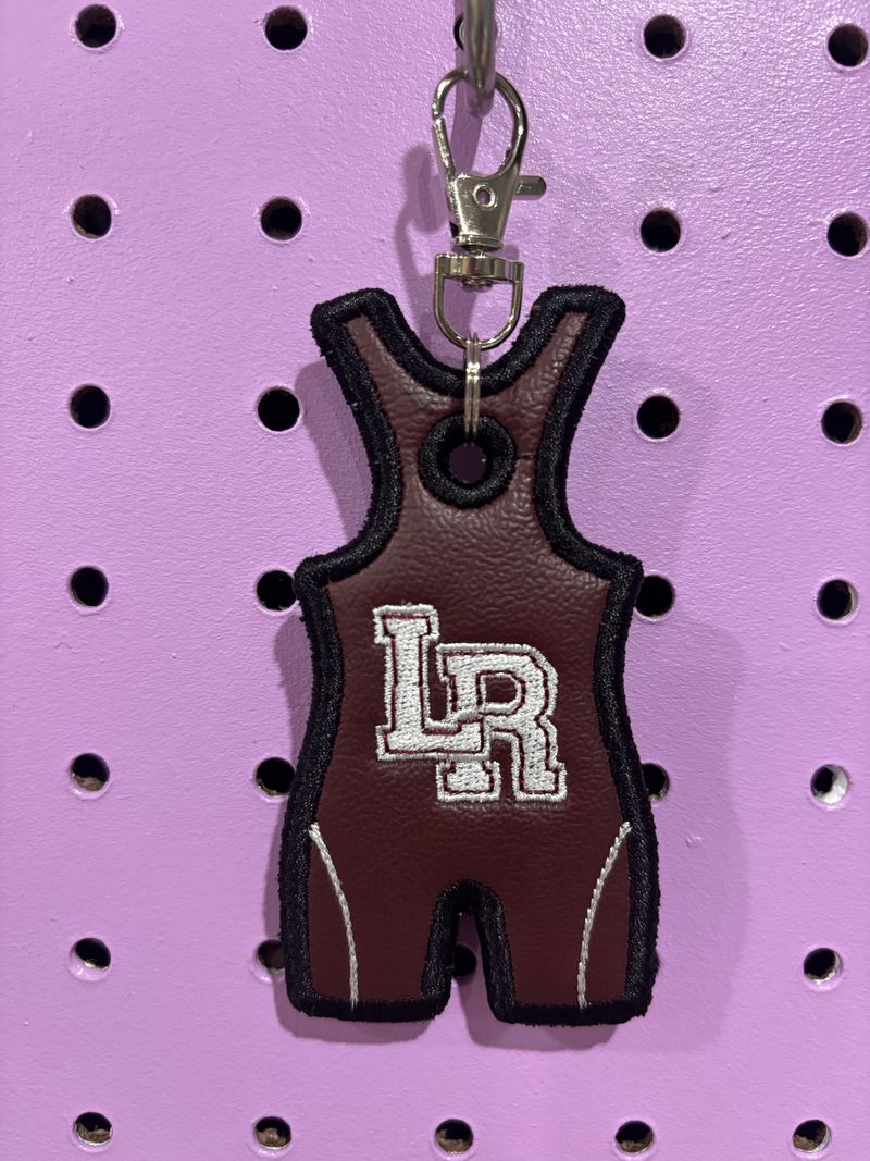 Maroon wrestling singlet bag tag with an embroidered LR logo, clipped to a purple pegboard