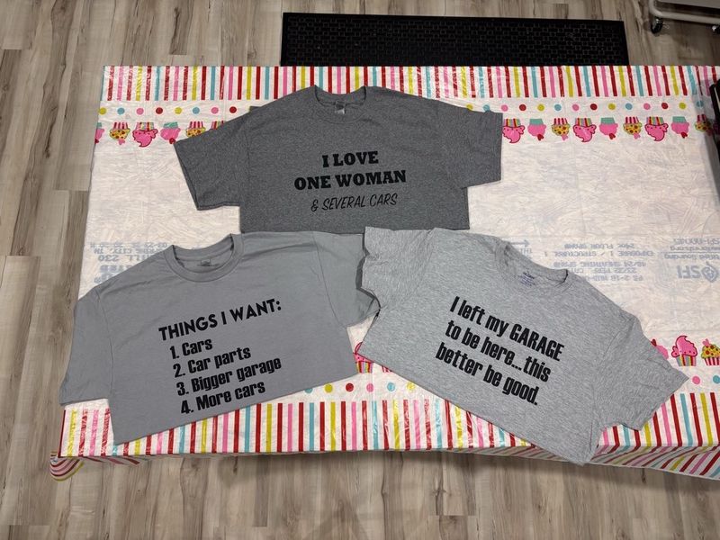 Three gray t-shirts with black heat transfer vinyl designs laid out on a table