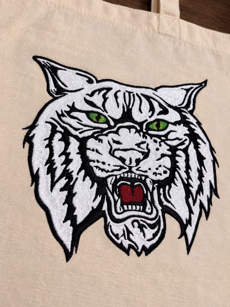 Canvas tote bag with a large white glitter thread wildcat head embroidered on the front