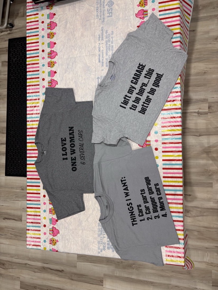 Three gray t-shirts with black heat transfer vinyl designs laid out on a table